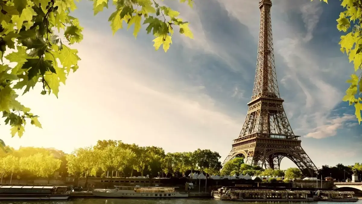 La tour Eiffel se détachant sur un ciel nuageux, entourée de feuillage