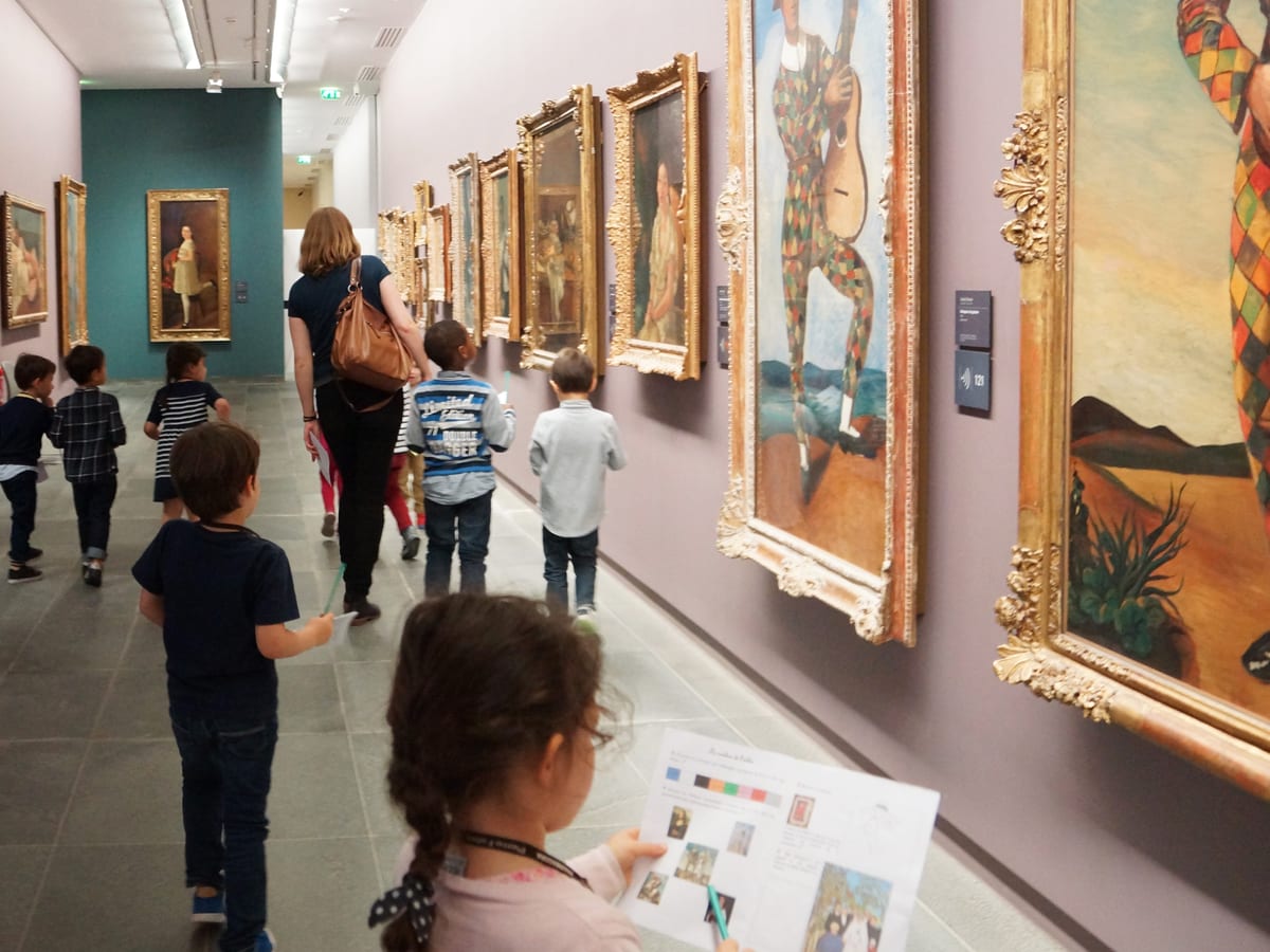 De jeunes élèves, un livret à la main, avancent dans une galerie de peintures