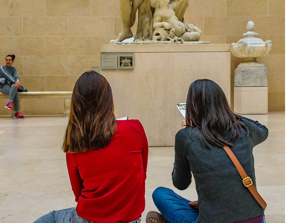 Deux étudiantes de dos prennent des notes devant une sculpture